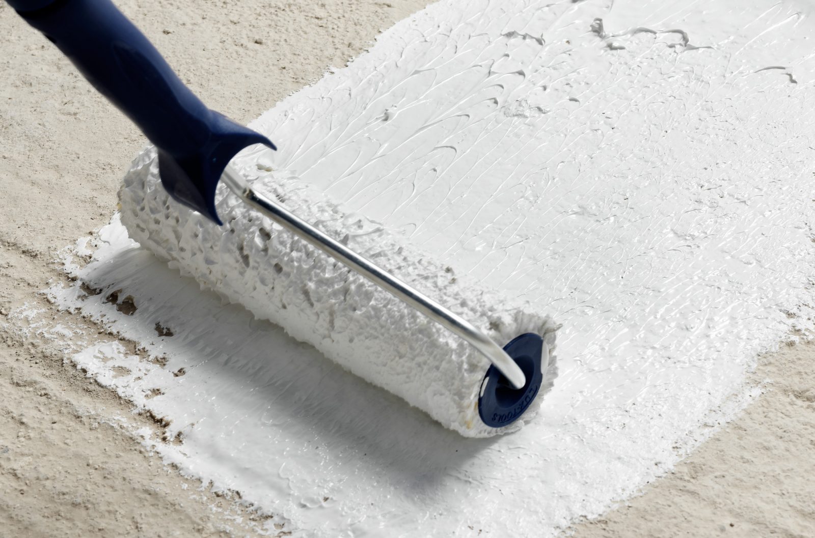 a paint roller applying monoflex tile adhesive ot a beige textured wall